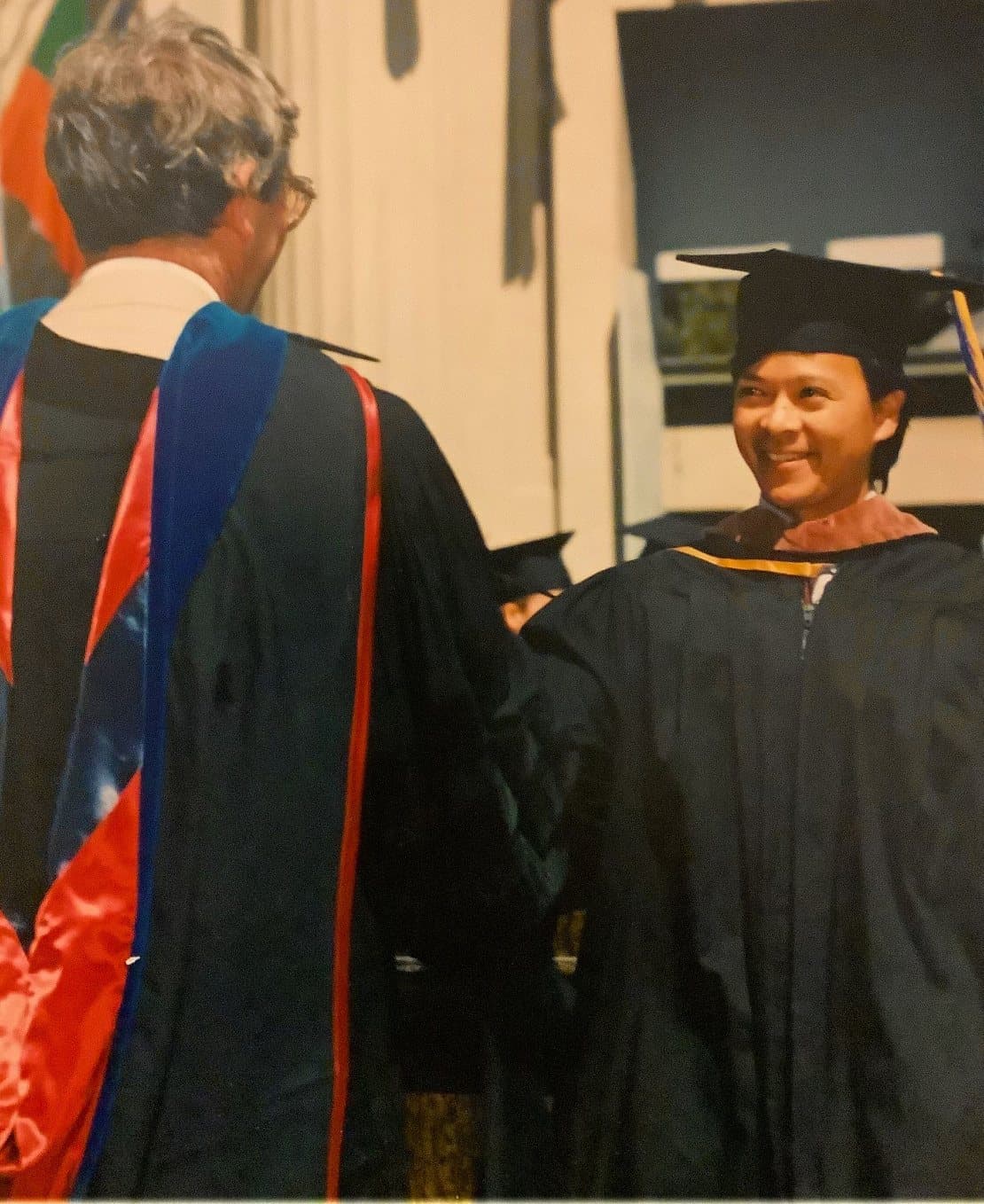 Tony Daysog in cap and gown, smiling as he shakes hands with a robed faculty member at his 1993 UC Berkeley graduation.