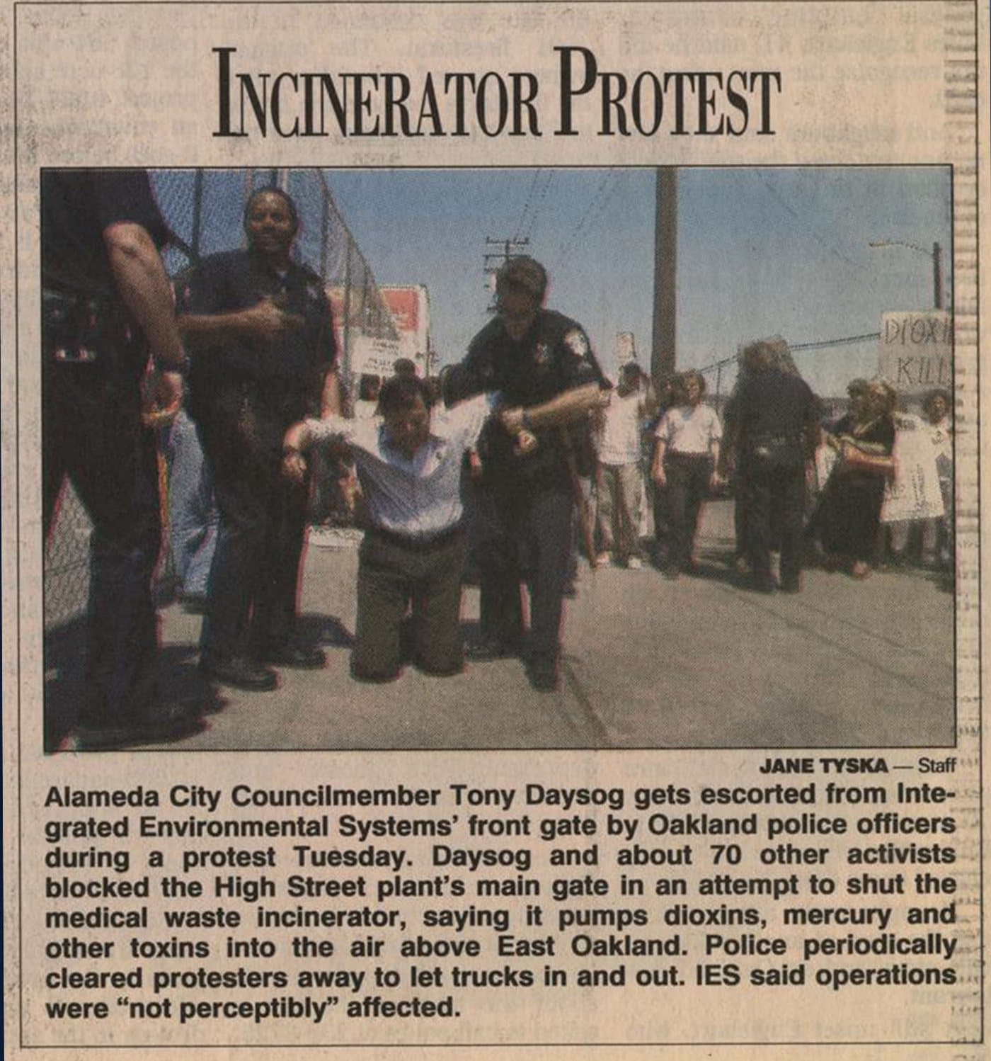 Newspaper photo headlined “Incinerator Protest”: Alameda City Councilmember Tony Daysog, on his knees, is escorted from Integrated Environmental Systems’ front gate by Oakland police officers during a protest in which he and about 70 other activists blocked the High Street medical waste incinerator.